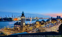 View of illuminated Landungsbrücken at dusk. In the background the Elbe with the container port.