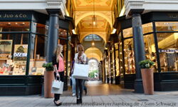 Two women with shopping bags talk on the pavement. A shopping arcade in the background.